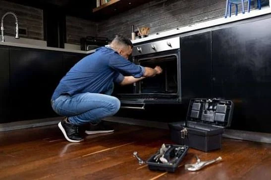 Technician servicing an oven in a dark kitchen
